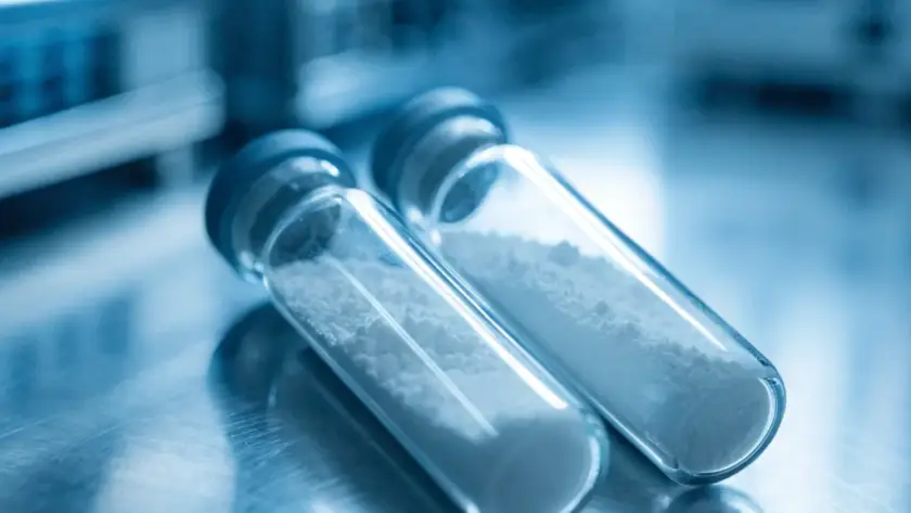 Two sterile glass laboratory vials containing pure lyophilized Retatrutide powder on a stainless steel workstation for in-vitro research.